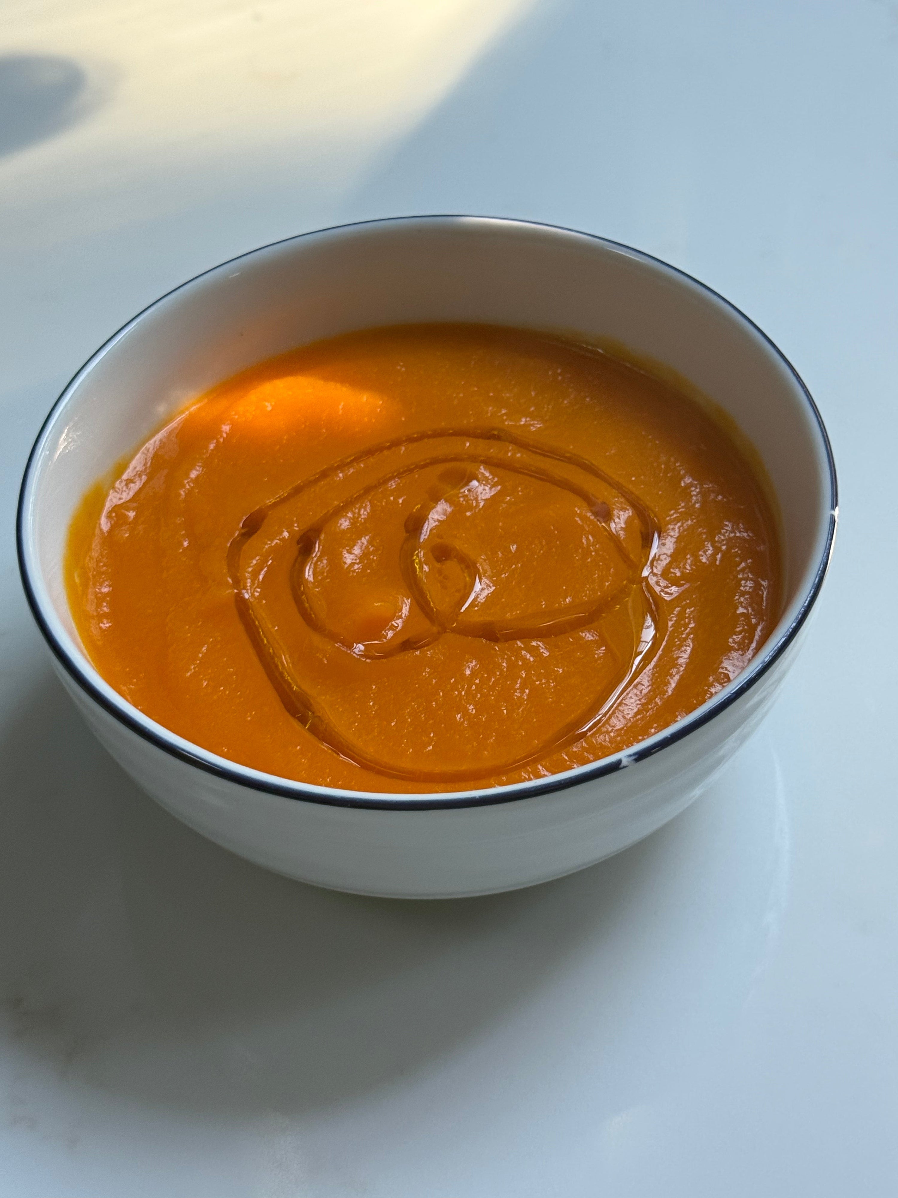 A bowl of creamy roasted butternut squash soup topped with a golden drizzle of BRISCA extra virgin olive oil
