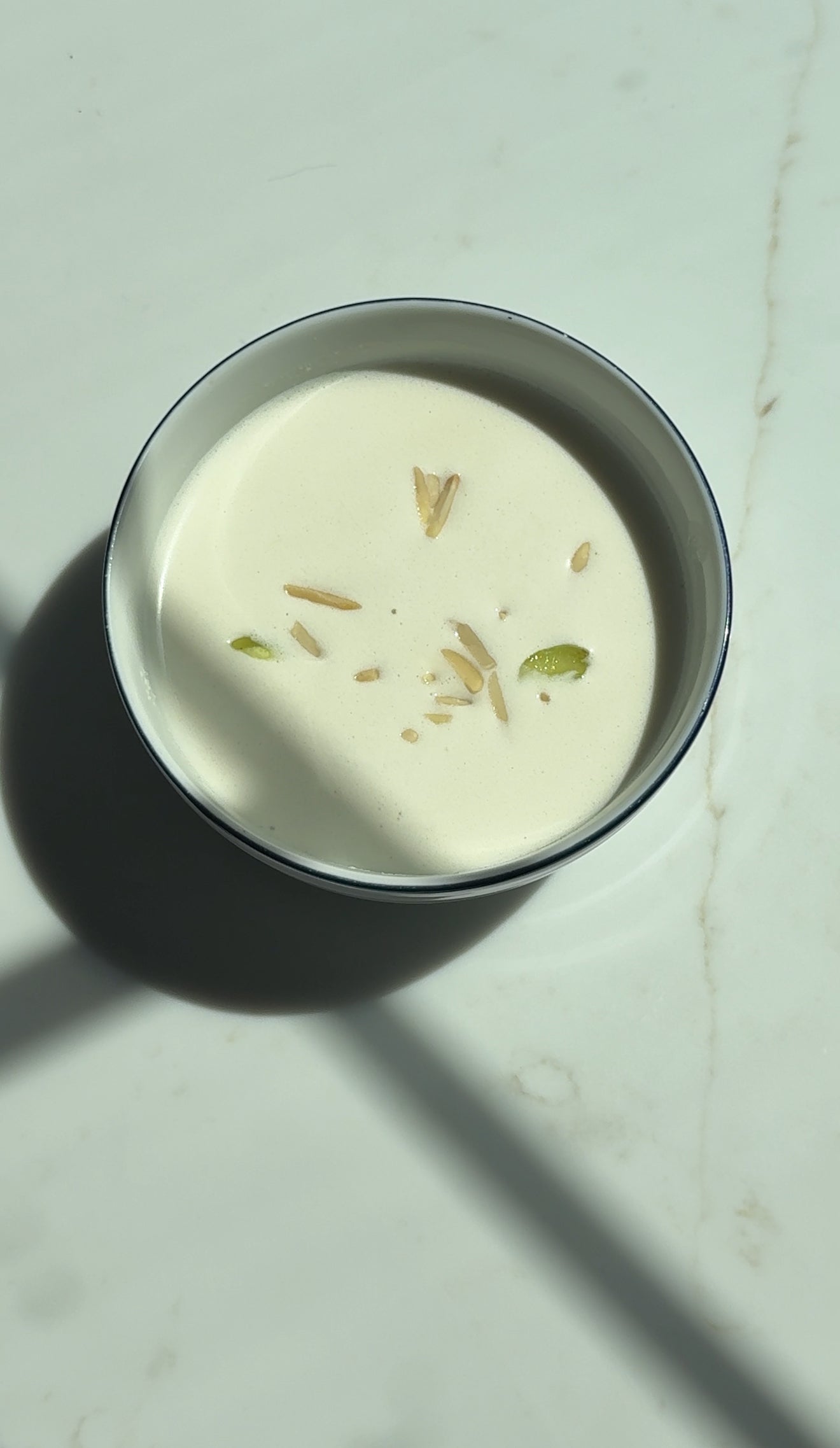 Ajoblanco, traditional Spanish cold almond soup, topped with grapes and almonds, served in a bowl on a white marble surface